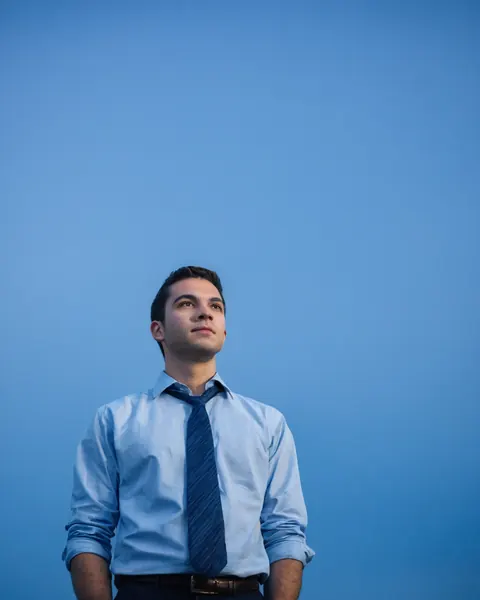A man in a blue shirt and tie looking up against a solid blue background.