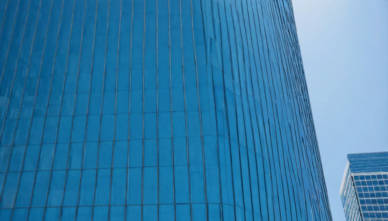 A tall blue glass building curves upward against a clear sky with another building nearby.
