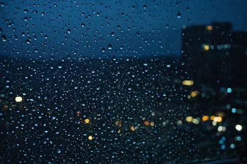 Raindrops on window glass with blurred city lights in background at night