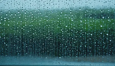 Raindrops sliding down a window with a green blurred background