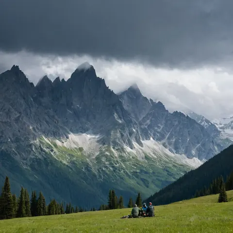Three people sitting on grass facing mountains under storm clouds