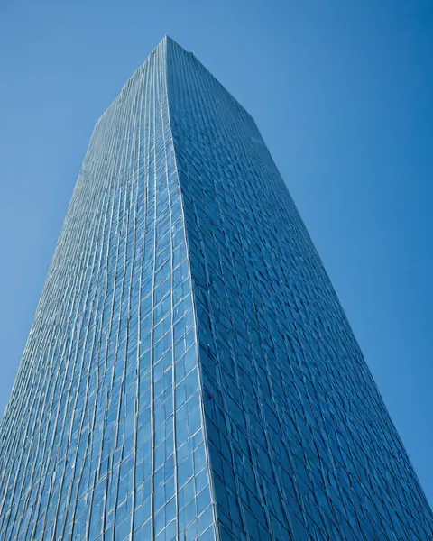 Towering glass skyscraper with vertical lines against clear blue sky