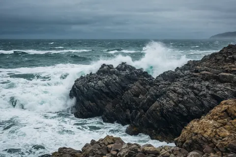 Waves crash against dark rocky cliffs under a stormy sky